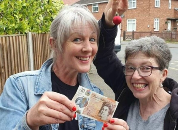 Two ladies holding a £10 note